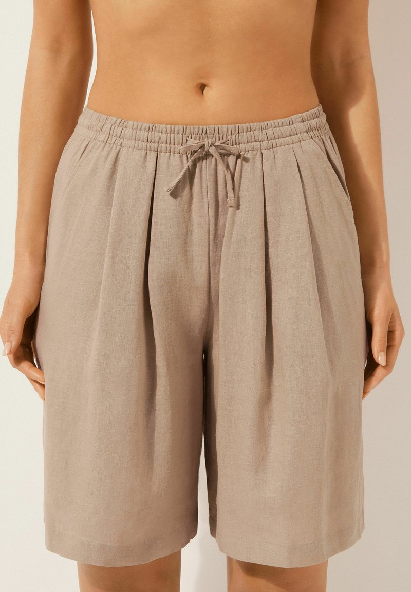 Pantalones cortos de lino marrón claro con cintura elástica, cordón y frente plisado. El diseño presenta un ajuste holgado y un corte a la altura de la rodilla.