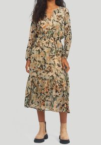 Långärmad, lager-på-lager klänning i ett lätt, genomskinligt tyg med ett camouflage-mönster i grönt, brunt och rosa, åtdragen vid midjan.