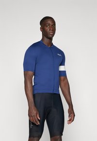 Navy Radtrikot mit kurzen Ärmeln, Reißverschluss vorne und weißen Akzenten an den Ärmeln, kombiniert mit schwarzen Radhosen mit gepolstertem Design.