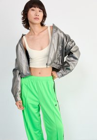 Silver cropped jacket with textured sleeves, paired with bright green track pants featuring black side stripes and zipper pockets.