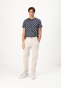Marineblå t-skjorte med et kremfarget geometrisk mønster, sammen med beige bukser og hvite sneakers. Slim-fit design, glatt tekstur.