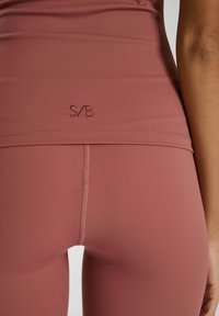 Leggings de cintura alta en color rosa suave, con un diseño sin costuras, costuras planas y un sutil logo bordado en la cintura.