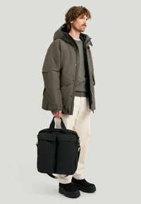 Puffjacka i mörkgrått, med huva och tryckknappar; matchas med en svart väska med dubbla blixtlåsfickor och justerbara handtag.