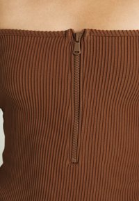 Hnědý ribrový top se středovým zipem, který má přiléhavý střih a hladkou texturu. Žádné další akcenty ani vzory.