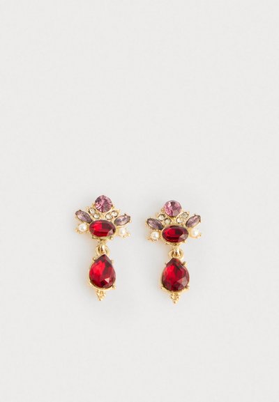 Boucles d'oreilles en or avec des pierres précieuses rouges en forme de goutte et ovales, des cristaux roses et transparents, et de petites perles sur un fond blanc.