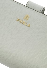 Lichtgrijze leren portemonnee met textuur en een gouden "Furla" logo. Heeft een gladde afwerking en verfijnde details in het interieur.