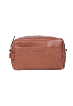 Brązowa skórzana kosmetyczka o prostokątnym kształcie, gładkiej fakturze, zamknięciu na zamek błyskawiczny oraz bocznej rączce; na froncie znajduje się wytłoczone logo.