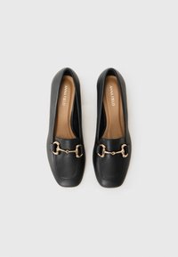Black leather loafers with a square toe, featuring a gold-tone hardware accent and a tan insole with brand logo. Smooth texture.