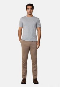 Grå t-shirt med korte ærmer, let stof, beige slim-fit bukser, glat tekstur, brune sko, enkelt design, minimal logodetalje på t-shirten.