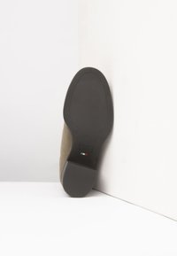 Scarpa in suede verde scuro con suola in gomma nera, punta leggermente appuntita e tacco piccolo. Dettaglio della bandiera italiana vicino alla suola.