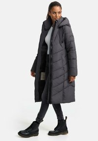 Long gray puffer coat with a hood, featuring a diagonal quilted design, front zipper closure, and side pockets. Paired with black combat boots.