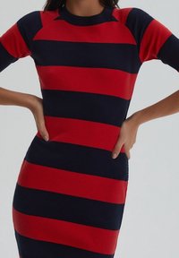 Robe côtelée à rayures rouges et bleu marine avec une coupe ajustée, des manches courtes et un col rond. Le tissu texturé ajoute un intérêt visuel.