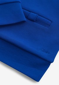 Plava dukserica s teksturiranim materijalom, rebrastim manžetama i prednjim džepom s diskretnim logotipom utisnutim na donjem rubu.