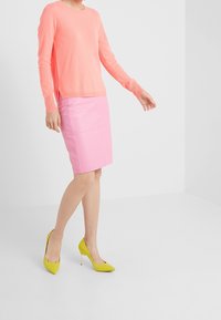 Gonna a matita in pelle rosa, maglione in knit rosa chiaro e scarpe con tacco giallo brillante, con una silhouette aderente e un design semplice.