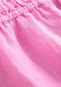 Närbild av rosa linne med synlig vävtextur och sydda rynkor i elastisk midja.