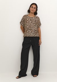 Leopard print short-sleeve top in beige and black, paired with loose black trousers. Textured fabric with relaxed fit and round neck.