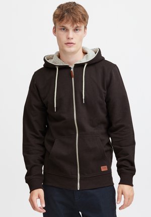 Bruine rits-hoodie met een fleece-gevoerde capuchon, trekkoordaccenten en zakken aan de voorkant. Bevat een klein merklabel aan de onderzijde.