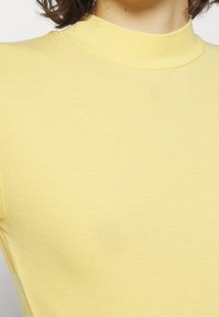 Gul ribbet turtle neck-top med et tætsiddende design, der har en høj krave og en glat tekstur, som fremhæver dens enkle, minimalistiske stil.
