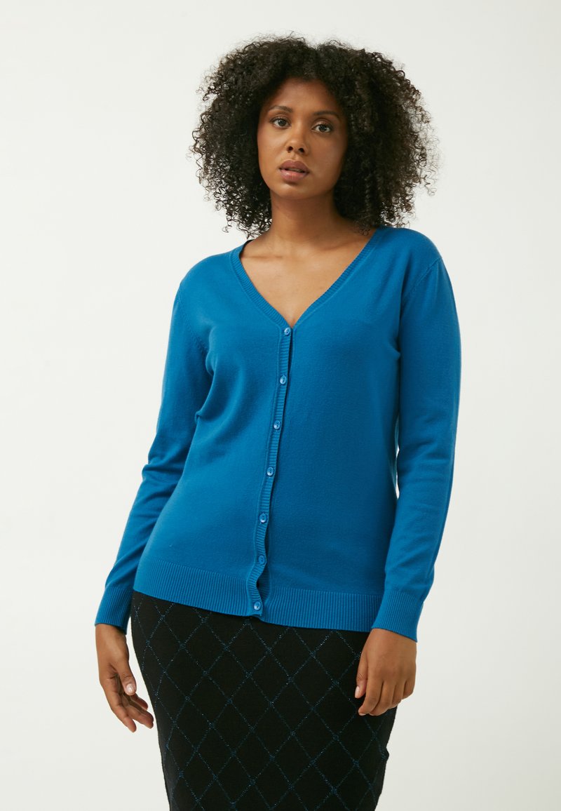 Cardigan bleu en tissu doux avec un col en V, des manches longues et une fermeture à boutons sur le devant. Poignets et ourlet côtelés.