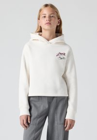 Manta-pear cropped hoodie creme com um bolso frontal e logotipo bordado. Material de algodão suave, mangas longas e capuz com cordão.