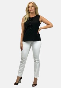 Czarna bezrękawnik z kwiecistymi akcentami na przodzie, w połączeniu z białymi dopasowanymi spodniami i czarnymi sandałami na obcasie z teksturowanym wykończeniem.