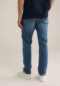 Svetlo modri traper hlače s ravnim krojem, ki imajo dva zadnja žepa in subtilno teksturirano površino, v kombinaciji z belimi športnimi copati.