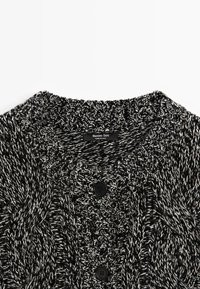 Cardigan nero e bianco lavorato a maglia con motivo a trecce testurizzato, collo ampio e tre bottoni neri sul davanti. Include un'etichetta del marchio.
