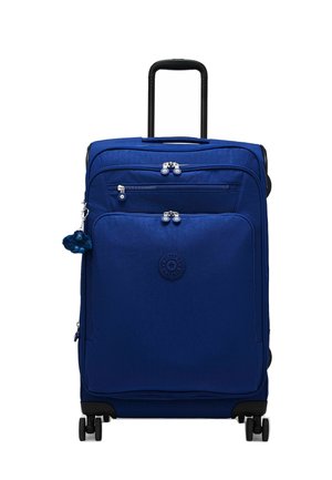 Valise souple bleue avec poignée télescopique, plusieurs compartiments zippés, quatre roues et un petit porte-clés en peluche attaché.