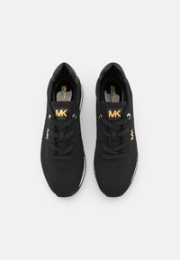 Para czarnych sneakersów Michael Kors z złotymi logo MK na języku i bokach, czarnymi sznurówkami oraz białymi podeszwami widzianymi z góry.