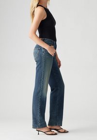 Džíny s vysokým pasem v modré barvě, rovný střih, s jemným vyblednutím a nezpracovaným lemem. Kombinováno s černým bezramínkovým topem a černými sandály.