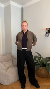 Pruun seemisnahast bomberjakk kraega kaeluse, luku ja kahe küljetaskuga. Sobitatud mustade laiade pükste ja mustade jalanõudega.