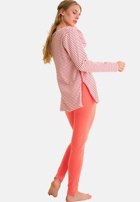T-shirt à manches longues rayé en rouge et blanc assorti à un legging corail uni. Le haut présente une coupe décontractée et des fentes sur les côtés.