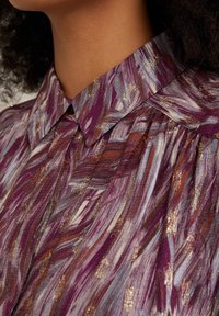 Purple and gray patterned fabric with metallic gold accents, featuring a classic collar and gathered detail at the neckline.