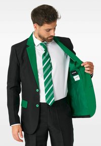 Schwarze Anzugjacke mit grünen Revers und Knöpfen, mit einem grünen Innenfutter. Kombiniert mit einem weißen Hemd und einer gestreiften grünen Krawatte.
