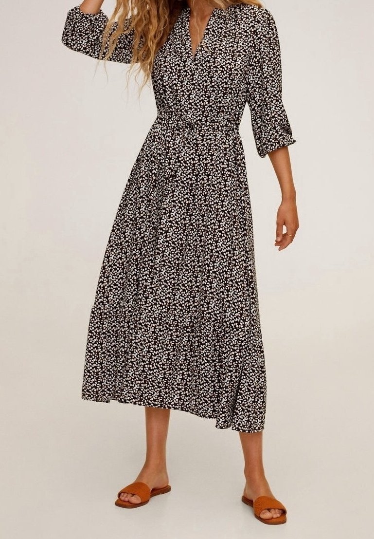 Robe midi noire à motif floral blanc, boutonnée sur le devant, avec des manches trois-quarts. Associée à des sandales plates marron.