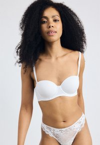 Soutien-gorge blanc rembourré avec des bretelles réglables et une texture lisse ; associé à une culotte blanche en dentelle présentant des motifs floraux et des bords festonnés.