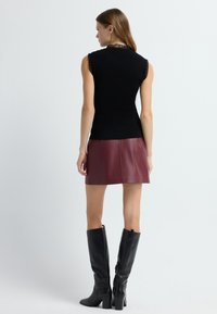 Bezramiączkowy czarny top z prążkowanego dzianiny z teksturowanym kołnierzem, w połączeniu z burgundową mini spódnicą z sztucznej skóry i czarnymi botkami na wysokości kolan na obcasie.