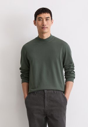 Dunkelgrünes, langärmliges Rollkragenshirt aus glattem Strickstoff, kombiniert mit grauen, vertikal gestreiften Hosen. Einfaches, klares Design.