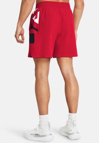 Pantalones cortos deportivos rojos con un logo en blanco y negro en el lateral, cinturilla elástica y tejido ligero. Espacio para transpirar en el dobladillo.