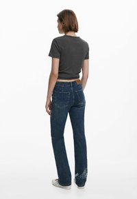Gray cropped t-shirt paired with blue flared jeans featuring back pockets and decorative embroidery at the hems. White sneakers complete the look.