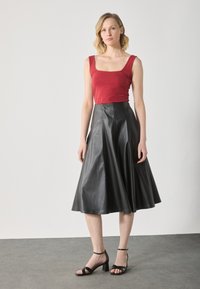 Rød, tettsittende tanktop kombinert med et knelengdes lærskjørt i svart. Skjørtet har en utsvingt design, med synlige sømmer og en jevn tekstur.