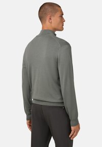 Sweat à mailles gris clair avec un col haut, des poignets côtelés et une coupe ajustée. Texture lisse, minimalisme dans les détails et aucune motif visible.