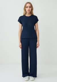 Navy-blaues Zweiteiler-Outfit mit einem kurzärmeligen Oberteil und weiten Hosen. Strukturiertes Material mit gewellten Kanten und lockerer Passform. Weiße Sneakers.
