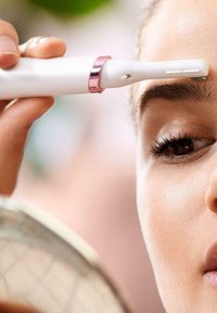 Tondeuse à sourcils fonctionnant sur batteries, avec un corps blanc et des accents dorés rose. Présente une forme mince et un bord de coupe fin pour plus de précision.