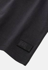 Czarna koszulka z prążkowanej tekstury, z teksturowaną czarną naszywką logo, na której widnieje napis "DOBRY NASTRÓJ OD 1982" blisko dolnej krawędzi.