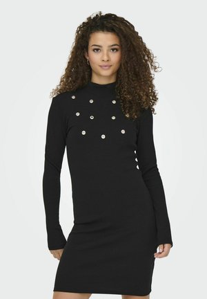 Must mustriga mustri kleit, millel on pikk varrukas ja mis on valmistatud kudumiskangast. Kleidil on mock neck ja esipaneelil on dekoratiivsed metallist nupud, mis on paigutatud mustrisse.