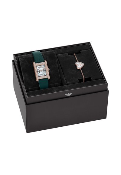 Een rechthoekig horloge met een groene band en een patroon op de wijzerplaat, naast een hartvormige armband van roségoud, geplaatst in een zwarte doos.