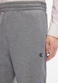 Joggers de algodón grises con cintura elástica, que presentan un pequeño logo negro bordado en el muslo. Textura suave y diseño ajustado.