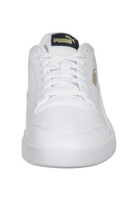 Białe sportowe buty z gładką skórzaną cholewą, sznurowanym wzorem i teksturowaną gumową podeszwą. Posiadają złote logo Pumy z boku.