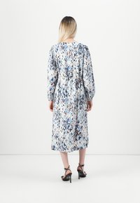 Floral midi dress featuring puffed sleeves, waist tie, and a colorful splatter pattern on a light background. Paired with black heeled sandals.